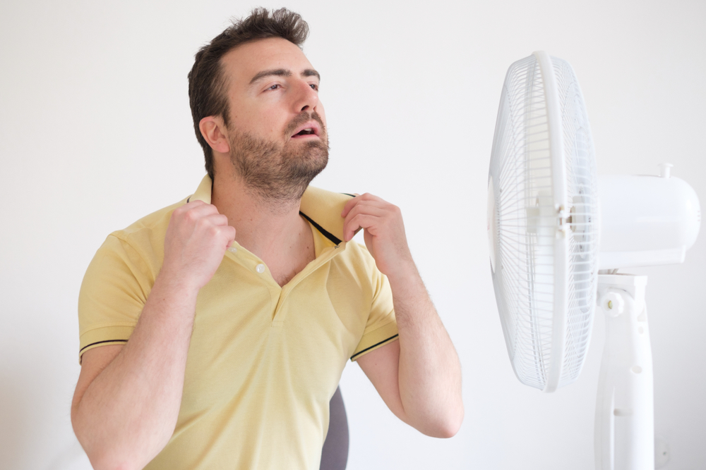 Man standing in front of a fan and pulling at his polo shirt to cool down