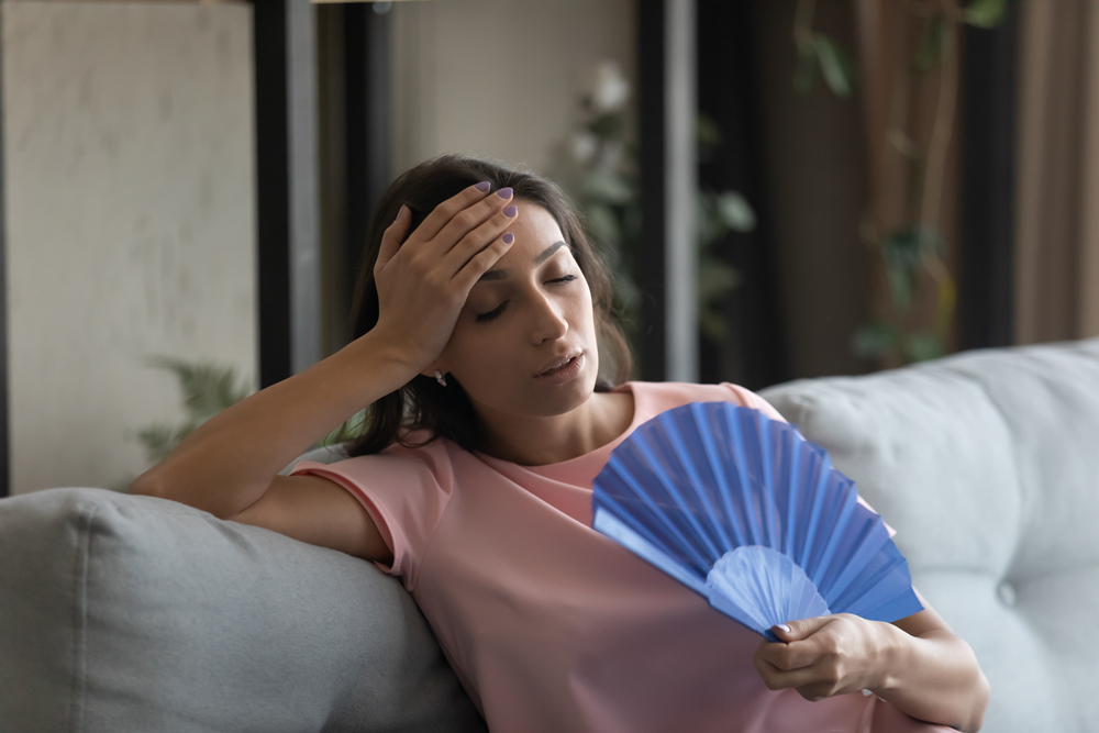 Woman sitting on the couch waving paper fan - humidity