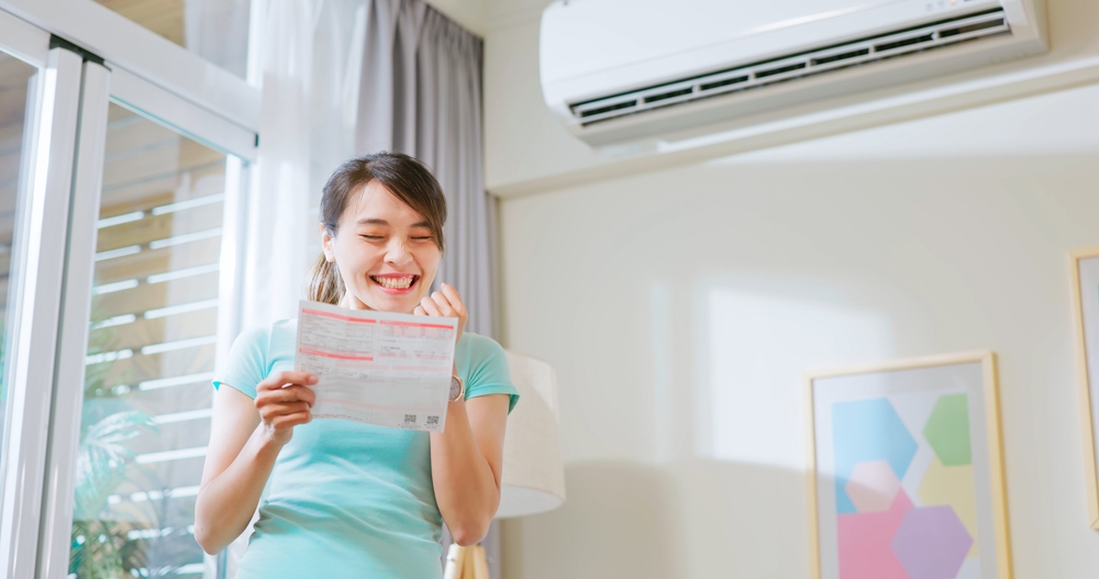 Woman smiling happily at power bills under air conditioner 
