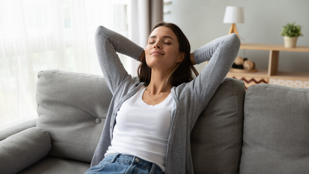 Woman kicking back on the couch with eyes closed and arms behind her head