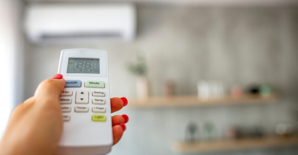 Hand with remote control directed at the split system air conditioner