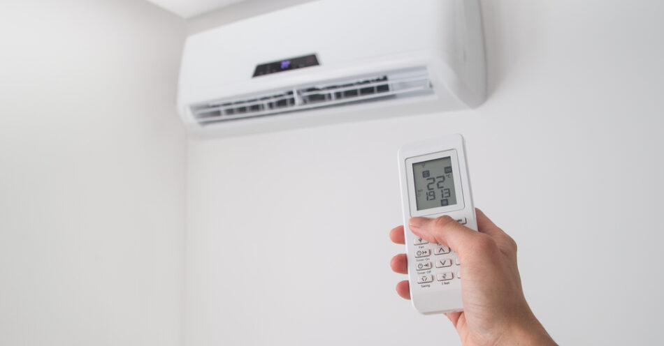 Hand holding a remote control pointed at a wall-mounted split system indoor unit