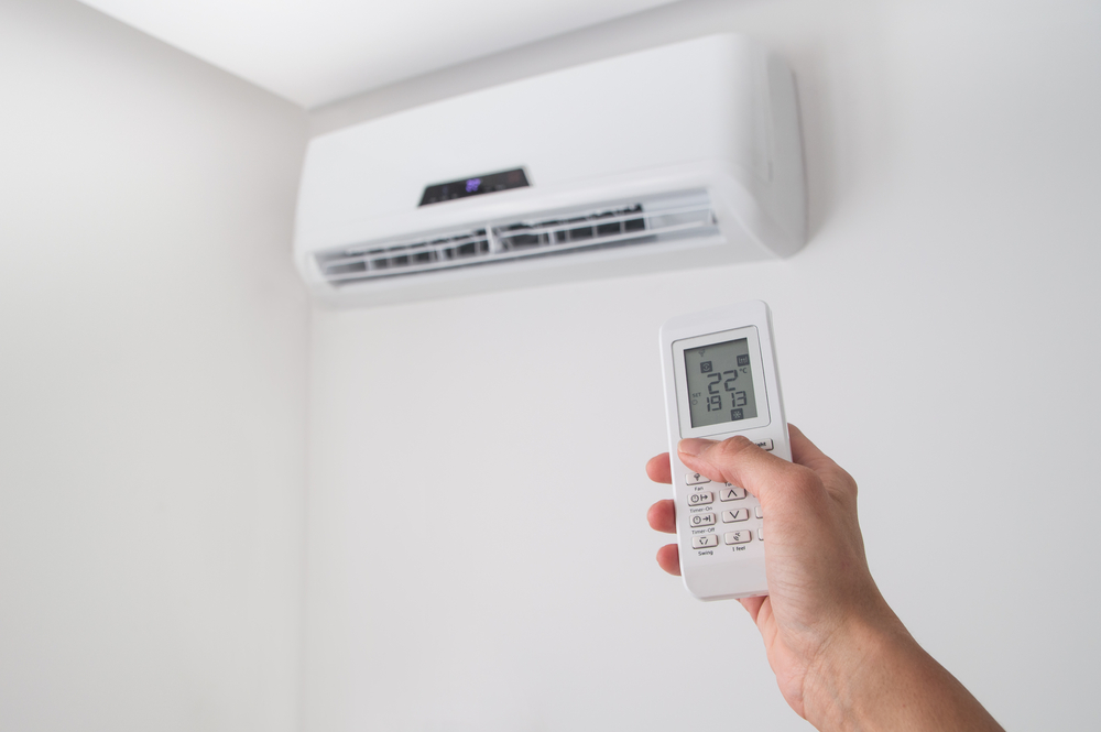 Hand holding a remote control pointed at a wall-mounted split system indoor unit