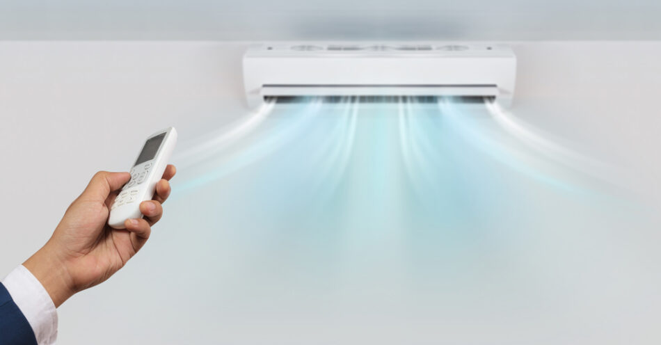 Wall hung split system air conditioner blowing out air, activated by a hand holding a controller