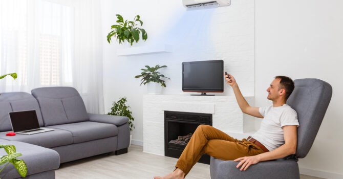 Man sitting on recliner turning on split system air conditioner with remote