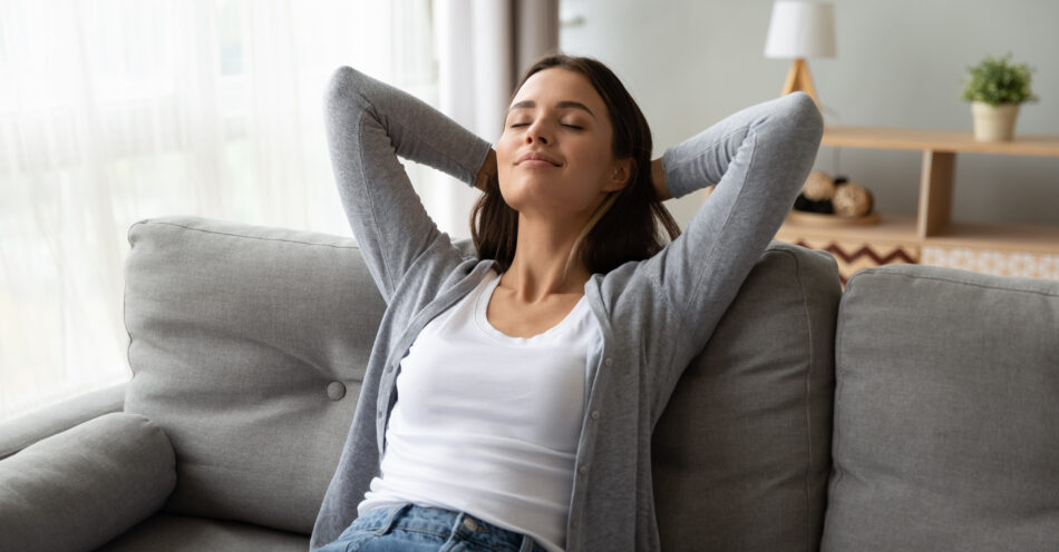 Woman lounging on her couch relaxing - eyes closed and arms behind her head