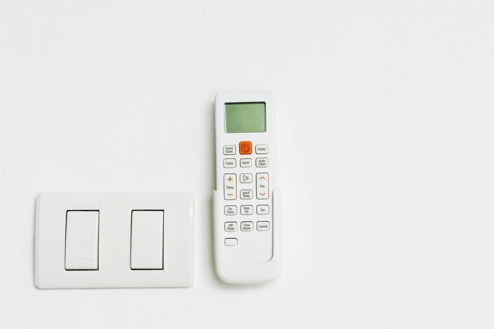 Air conditioning remote next to light switch on white wall