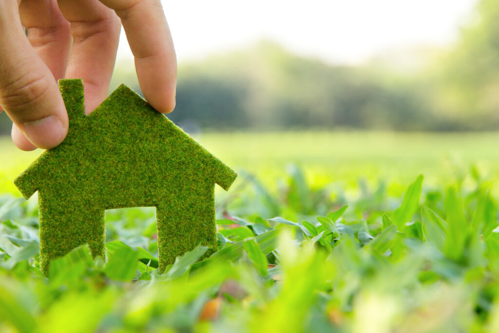 Eco friendly home concept: A hand places a green house cut-out in the grass