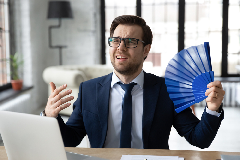 Overheated office employee waves a folding fan at his desk