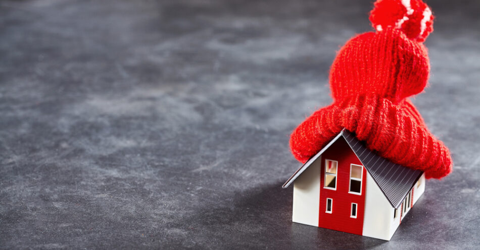 Small toy house with a red knitted hat on its roof - Representing home heating