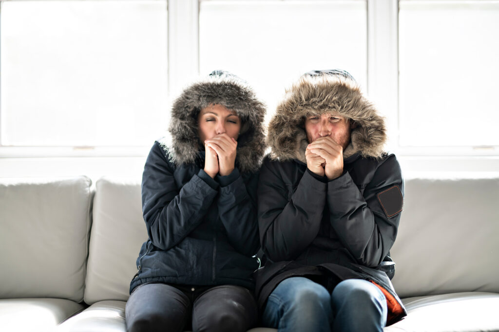 Cold couple sitting on the couch wearing winter coats with furry hoods