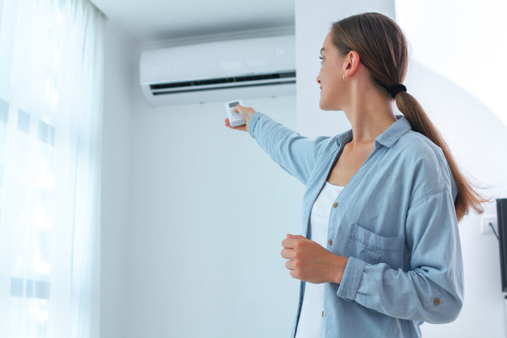 Young woman pointing AC remote around the corner and adjusting high-wall split system