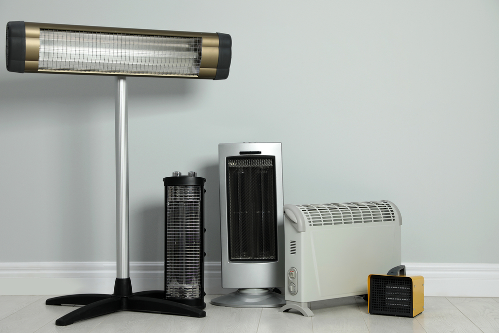 Different types of space heaters in front of a grey wall.
