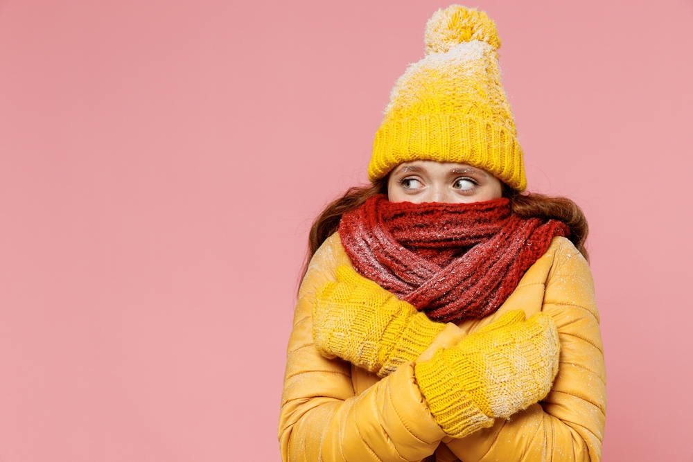 Cold woman in a yellow jacket, hat, and mittens with red scarf.