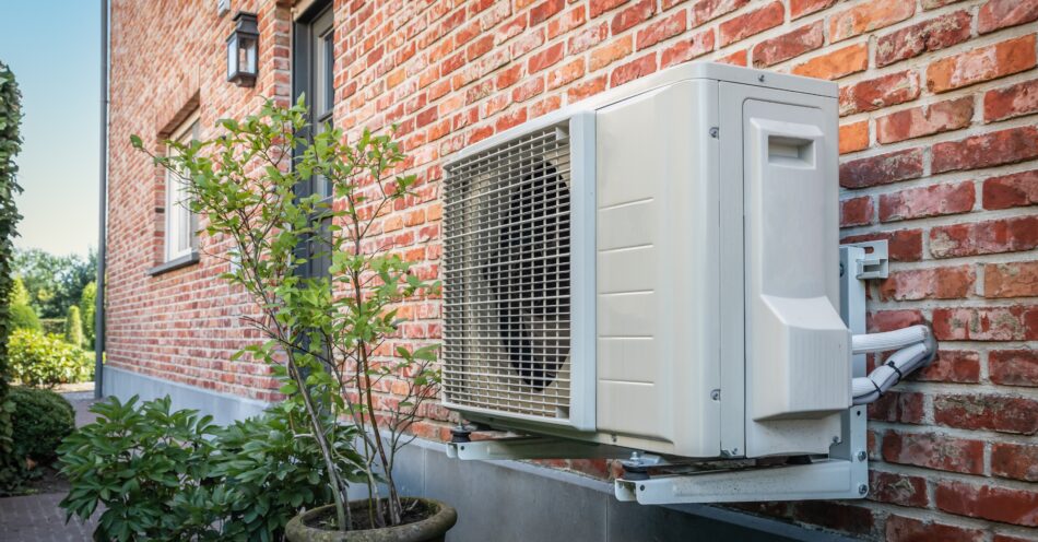Outdoor unit of an HVAC system, with a tree growing nearby, representing the sustainable benefits of an electric system.