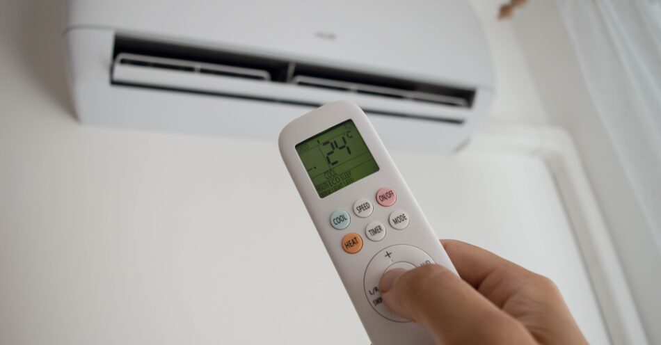 Ductless split system on a wall, with a hand holding a remote adjusting the temperature.